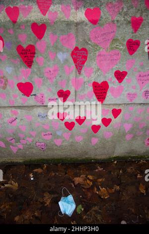 Una maschera è vista a sinistra sotto i cuori rossi, che rappresentano coloro che sono morti di Covid-19, sul National Covid Memorial Wall lungo il Tamigi a Londra. Foto Stock