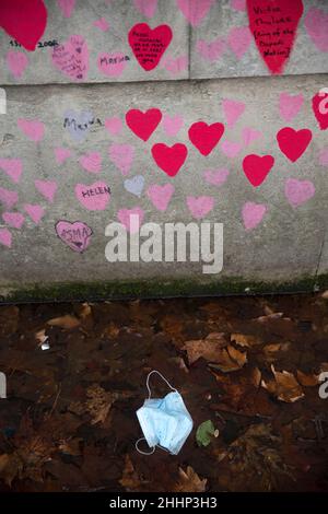 Una maschera è vista a sinistra sotto i cuori rossi, che rappresentano coloro che sono morti di Covid-19, sul National Covid Memorial Wall lungo il Tamigi a Londra. Foto Stock