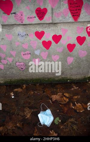 Una maschera è vista a sinistra sotto i cuori rossi, che rappresentano coloro che sono morti di Covid-19, sul National Covid Memorial Wall lungo il Tamigi a Londra. Foto Stock