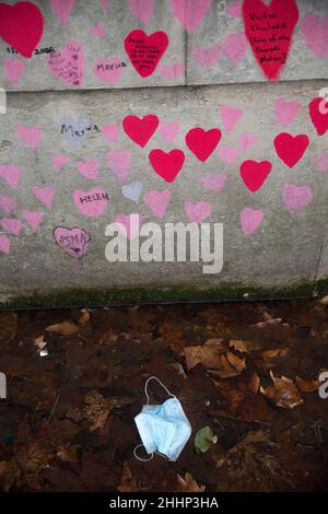 Una maschera è vista a sinistra sotto i cuori rossi, che rappresentano coloro che sono morti di Covid-19, sul National Covid Memorial Wall lungo il Tamigi a Londra. Foto Stock