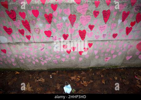 Una maschera è vista a sinistra sotto i cuori rossi, che rappresentano coloro che sono morti di Covid-19, sul National Covid Memorial Wall lungo il Tamigi a Londra. Foto Stock