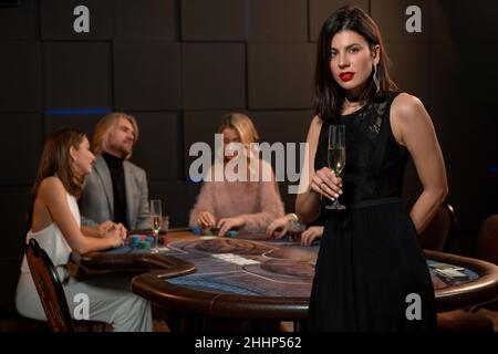 Bella giovane brunetta con bicchiere di champagne accanto al tavolo da poker Foto Stock