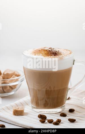 Caffè latte versato a strati con schiuma e un piano croccante al cioccolato su un tavolo da cucina leggero. Immagine verticale con spazio di copia. Foto Stock