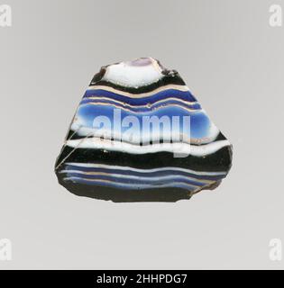 Mosaico di vetro dentellato frammento di ciotola fine 1st secolo a.C.–inizio 1st secolo d.C. frammento di corpo romano.traslucido viola profondo che appare nero, blu cobalto, e bianco opaco.collo in uscita; Lato leggermente curvo rastremato verso il basso.motivo a mosaico a nastro formato da sezioni di una canna singola in viola macinato con fili irregolari ondulati bianchi e blu in linee orizzontali parallele; all'esterno, tre nervature verticali poco profonde, abbastanza distanziate, con sommità appiattita e bordi esterni arrotondati.interno lucido; vaiolatura di bolle di superficie e crepe all'interno; sbucciature e macchie di crema iridescente erbaccia Foto Stock
