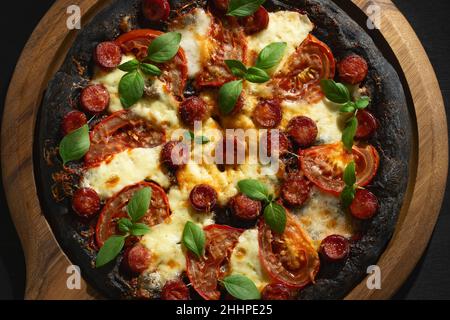 Pizza nera con pomodori, salsicce, mozzarella e basilico. Impasto con polvere di carbone di bambù sano. Foto Stock