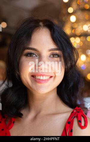 Ritratto di sorridente giovane donna dai capelli scuri con pelle bianca con luci dietro con labbra a rilievo e occhi espressivi Foto Stock