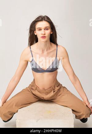 Giovane donna sottile con capelli lisci scuri isolati sul beige con gambe separate Foto Stock