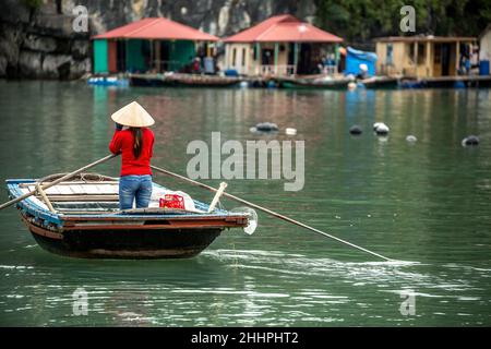 Donna di canottaggio canotto in legno e case galleggianti, Vung Vieng villaggio di pescatori, la baia di Ha Long, Bai Tu Long Settore, vicino a Ha Long, Vietnam Foto Stock
