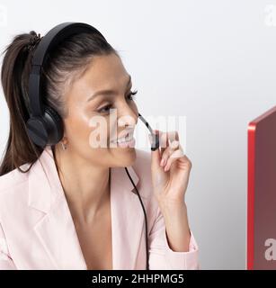 Inghilterra, Regno Unito. 2021. Donna attraente che indossa una cuffia telefonica e una giacca rosa. Foto Stock