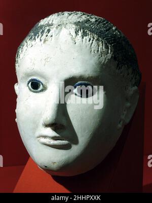 Maschera di una donna con i capelli arrotolati alla fronte e templi A.D. 150–200 periodo romano le maschere in gesso derivano da tradizioni faraoniche, in cui la maschera serviva come sostituto della testa del defunto e come mezzo per elevarlo allo stato immortale. La derivazione si riflette spesso in dipinti e testi situati sul mantello che circonda la testa. Come i ritratti di mummia dipinta, le maschere suggeriscono apparenze fortemente individualizzate e influenzano le mode romane in acconciatura, gioielli e vestito. Seguono, tuttavia, un modello un po' diverso. Ad esempio, ma femmina Foto Stock
