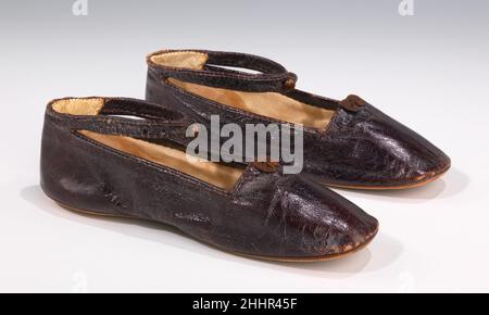 Scarpe 1850–69 europeo queste eleganti pantofole sono essenzialmente una versione miniaturizzata di uno stile adulto, ma includono una caviglia-cinghia integrale, rendendole così adatte per un bambino. La piccola prua, le raffinate tubature in pelle e il bottone metallizzato sono elementi piacevoli che mostrano l'attenzione al dettaglio. Il bambino di bronzo è stato usato ampiamente durante la seconda metà del 19th secolo per le scarpe da donna. Il caratteristico colore marrone violaceo con lucentezza metallica o iridescente è stato prodotto tintando la pelle con cocineale, un colorante rosso prodotto dalla frantumazione dei corpi essiccati dell'insetto Dactylopio coccus Foto Stock