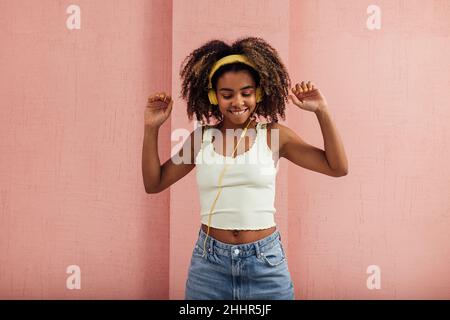 Donna allegra in cuffie gialle che si godono la musica alzare le mani Foto Stock