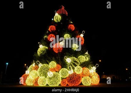 Un albero di Natale in una piazza della città di notte, decorato con grandi palline colorate Foto Stock