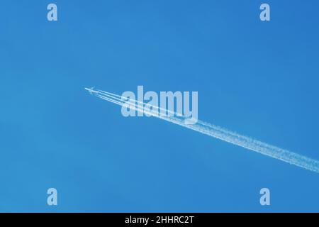 Jet Airliner vola in alto nel cielo, lasciando contraglie nel cielo azzurro chiaro Foto Stock