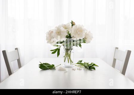 peonie bianche in vaso e foglie cadute su un tavolo bianco d'annata - spazio copia Foto Stock