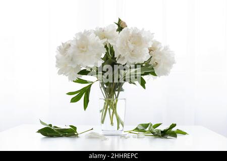peonie bianche in vaso e foglie cadute su un tavolo bianco d'annata - spazio copia Foto Stock