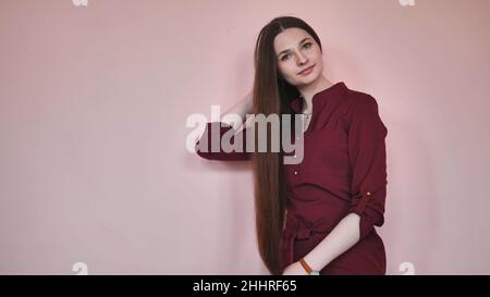 Ragazza dai capelli lunghi pettina i capelli su uno sfondo rosa. Foto Stock