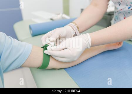 Esecuzione di un esame del sangue da una vena nella sala di trattamento. Infermiere che tira una siringa con un ago nella mano del paziente. Tampone premuto contro Foto Stock