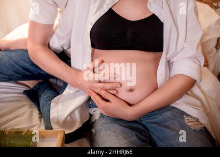 Concetto di gravidanza e maternità, unità della famiglia. Una bella donna incinta tiene il ventre dal basso e dal lato superiore. Lei mette le mani su Foto Stock