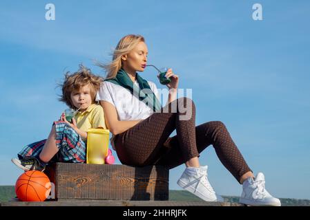 Madre e figlio si rilassano dopo lo sport. Giovane donna con bambino che indossa abiti sportivi che bevono frullato dopo l'allenamento all'aperto. Bevanda proteica per la salute. Foto Stock