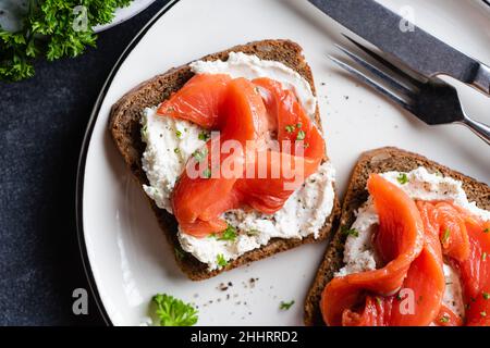 Pane tostato di segale con formaggio cremoso e salmone su un piatto vista dall'alto. Salutari antipasti o spuntini, sandwich all'aperto Foto Stock