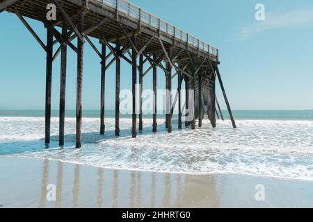 Molo che sporge da una spiaggia bagnata e sabbiosa nell'Oceano Pacifico a San Simeon, California Foto Stock
