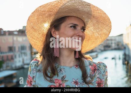 Felice giovane donna turistica solista in abito floreale con visita del cappello sul ponte dell'Accademia a Venezia. Foto Stock