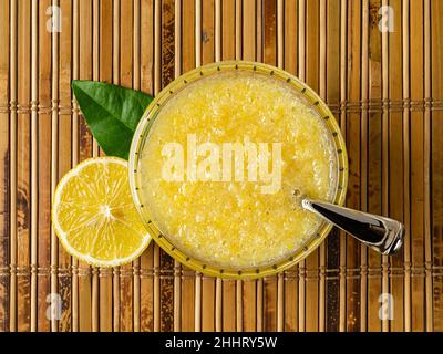 Vista dall'alto della marmellata del congelatore del limone in una ciotola sopra il tappeto del tavolo di bambù. Marmellata fresca fatta senza cuoco di limoni succosi mescolati con lo zucchero. Purea di acido amidacea. Foto Stock