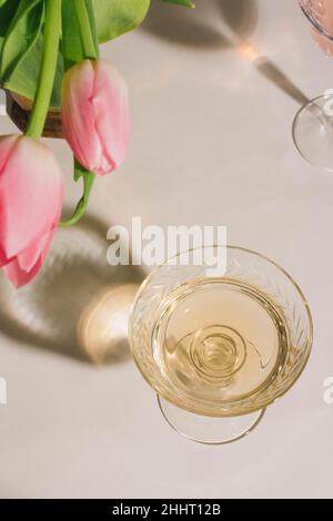 tulipani rosa in vaso di ottone e vino bianco cocktail bevanda in bicchiere coupé su sfondo bianco Foto Stock