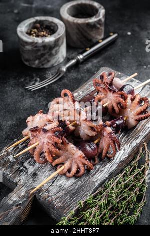 Spiedini con mini polpi grigliati. Sfondo nero. Vista dall'alto Foto Stock
