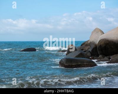 Paesaggio delle onde del mare che si avvicina fortemente alle rocce con un lotto di schiuma nel Parco Tayrona, Colombia Foto Stock