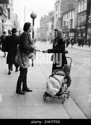 Un venditore di giornali femminile a Liverpool, vendendo una copia del Daily Post ad una madre in Street.Circa 1940. Foto Stock