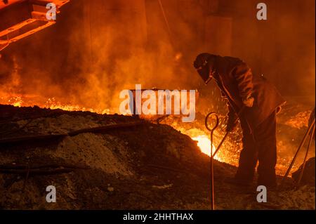 Il processo di rilascio di ghisa da un altoforno. Un uomo lavora con metallo fuso Foto Stock