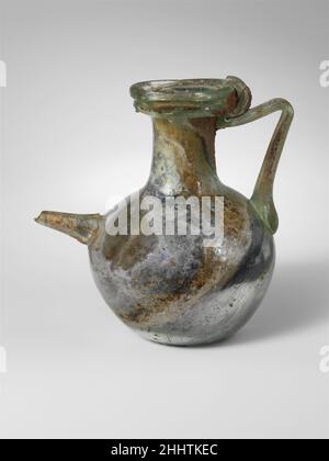 Bottiglia di vetro spouted fine 2nd–4th secolo d.C. romana traslucido verde azzurro pallido, con manico dello stesso colore, beccuccio e bordo trail.thick, piegato sopra e dentro; bocca svasata; collo cilindrico, che si espande alla base per unire il corpo globulare; calcio basso nel fondo; beccuccio dritto, rastremato ad una punta arrotondata a fuoco, fissato ad angolo al corpo superiore sul lato opposto al manico; Manico di asta, applicato come un tampone spesso al corpo superiore, tirato su e verso l'esterno, poi girato dentro ad un angolo acuto e trainato sulla parte superiore del collo, sopra la pista ed all'esterno del bordo di RIM.Below, un singolo sentiero solido ha avvolto il collo leggermente sopra 1½ volte b Foto Stock