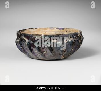 Ciotola in vetro costato 1st secolo a.C. Greco, Mediterraneo orientale traslucido profondo miele marrone.bordo leggermente invertito con bordo esterno smussato; lati curvati verso piatto ma leggermente disuguale bottom.on interno, due ampie scanalature orizzontali tagliate in una fascia sotto il bordo; Sull'esterno, diciotto nervature inclinanti prominenti con le parti superiori arrotondate e rastremantesi verso bottom.intact; bolle del pinprick; vaiolatura profonda e iridescente brillante che intemperia sull'esterno, e tempo cremoso spesso che copre la maggior parte dell'interno. Vaschetta in vetro a coste 248935 Foto Stock