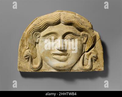 Terracotta gorgoneion antefix (tegole) 2nd metà del 5th secolo a.C. Greco, Italiano del Sud, Tarentino lo stile di questo antefix gorgoneion è di tipo transitorio tra l'arcaica, più feroce Medusa e la calma Medusa dei secoli successivi. Tracce di scivolamento bianco rimangono sul suo viso, e alcune tracce di vernice dai capelli gialli una volta luminosi possono ancora essere viste sulla sua testa. Le iridi dei suoi occhi sarebbero state dipinte blu o nero. Terracotta gorgoneion antefix (tegole). Greco, Italiano del Sud, Tarentine. 2nd metà del 5th secolo a.C. Terracotta. Classico. Terracotte Foto Stock