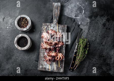 Spiedini con mini polpi grigliati. Sfondo nero. Vista dall'alto Foto Stock