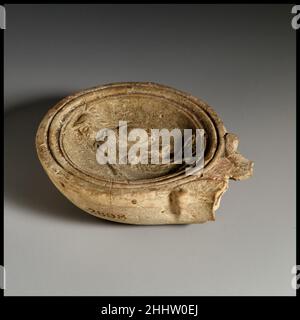 Lampada ad olio di terracotta 1st metà del 1st secolo d.C. romana, cipriota Loeschcke tipo 1B. Realizzato in stampo. Disco: figura di Athena, drappeggiato, rivolto verso sinistra, indossando una crestata, tenendo la lancia trasversale nello scudo destro e rotondo nella mano sinistra, con un'ampia banda di linee e scanalature verso il bordo. Ugello a spirale. All'interno dell'anello di base rialzato, base piatta, con grandi lettere impressi al centro: FVAS.corpo intatto, ma la maggior parte dell'ugello manca. Lampada ad olio di terracotta. Romano, cipriota. 1st metà del 1st secolo d.C.. Terracotta. Prima imperiale. Terracotte Foto Stock