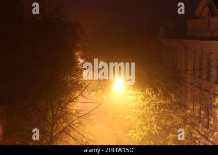 Vista sulla strada dalla camera in una serata d'autunno con nebbia. Una luminosa lanterna illumina gli antichi edifici della strada. Foto Stock