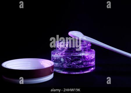 vaso trasparente con gel di colore viola idratante su sfondo nero Foto Stock