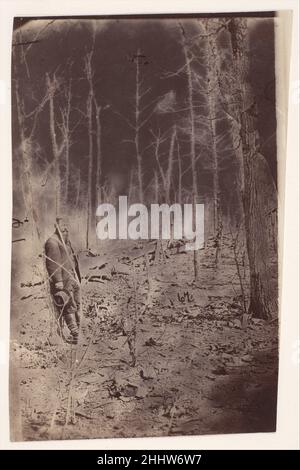 [The Wilderness Battlefield, Near Spotsilvania, Virginia] 1865 (?) Sconosciuto la battaglia della Wilderness è stata combattuta 5-7 maggio 1864, nella stessa foresta della Virginia disputata un anno prima nella campagna di Chancellorsville. Quando i soldati presero le loro posizioni nei boschi, il terreno era già cosparsi di teschi. Il paesaggio densamente boscoso rendeva impossibile la guerra di campo convenzionale. L'artiglieria era tutt'altro che inutile. Il fuoco del moschettio schitò e strinse gli alberi giovani. La fitta sottobosco di brambles spinosi, addensamenti e radici, che renivano difficili da costruire le difese della terra, non poteva a sua volta fermare st Foto Stock