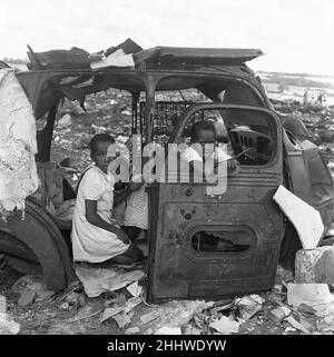 I bambini delle cittadine di Langa e Windermere sono stati visti qui per scovare la punta dei rifiuti di Orlando vicino a Città del Capo. I bambini cercano ombra dal sole di mezzogiorno in un relitto di una macchina 4th febbraio 1955 Foto Stock