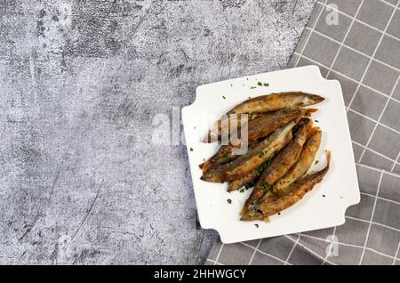 Pan il capelin fritto o il pesce odorato su una piastra quadrata bianca su uno sfondo scuro. Vista dall'alto, disposizione piatta Foto Stock
