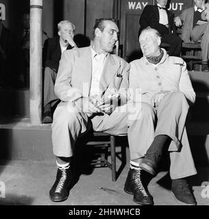 Primo Carnera, attore e wrestler professionista, anche un ex boxer professionista, ritratto durante la pausa dalle scene di ripresa per il nuovo film, A Kid for Two Farthings, a Shepperton Studios, Surrey, Inghilterra, 13th settembre 1954. L'insieme è una rappresentazione di un anello di wrestling a Londra Est. Suona Python Macklin. Nella foto, parlando con 'Bombardier' Billy Wells, British e British Empire Boxing campione dal 1911 al 1919. Foto Stock