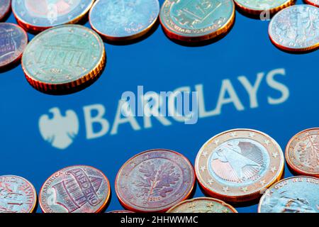 Varietà di monete metalliche sullo sfondo del logo della banca Barclays Foto Stock