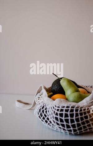 Una varietà di frutta in una borsa eco-aware si trovano sul tavolo. Superficie piana sana con spazio per la copia. Avocado, limoni, pesche, pere, arance. Foto Stock