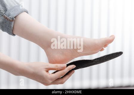 Donna soletta ortopedica da interno, da vicino. Ragazza che tiene una soletta accanto al piede a casa. Solette ortopediche. Striscione per la cura del piede. Piedini piatti Foto Stock