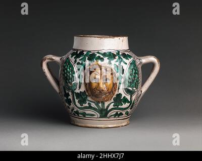 Vaso a due maniche con teste dei leoni all'inizio del 15th secolo italiano questo vaso, realizzato all'inizio del XV secolo, include ornamento in rilievo audace di coni di pino o uva e impressionanti maschere di leone. Può essere stato fatto vicino a Firenze, o più a sud vicino alle città di Viterbo o Orvieto. Vaso a due maneggiate con teste Lions 467634 Foto Stock