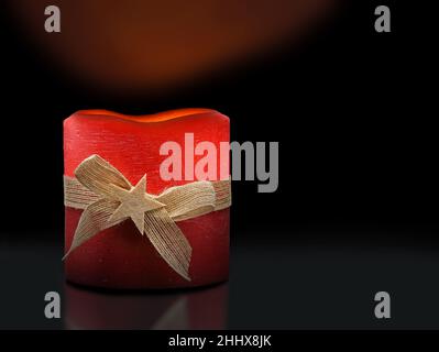 candela di natale rosso acceso con banda di iuta e stella su sfondo nero, illuminato decorazione di natale Foto Stock