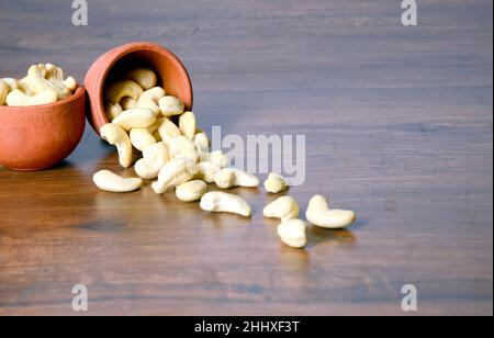 Arachide crude arrosto salate in una ciotola di legno su un tavolo rustico, sano spuntino vegetariano, anacardium occidentale, anachide su sfondo bianco, anachide. Foto Stock